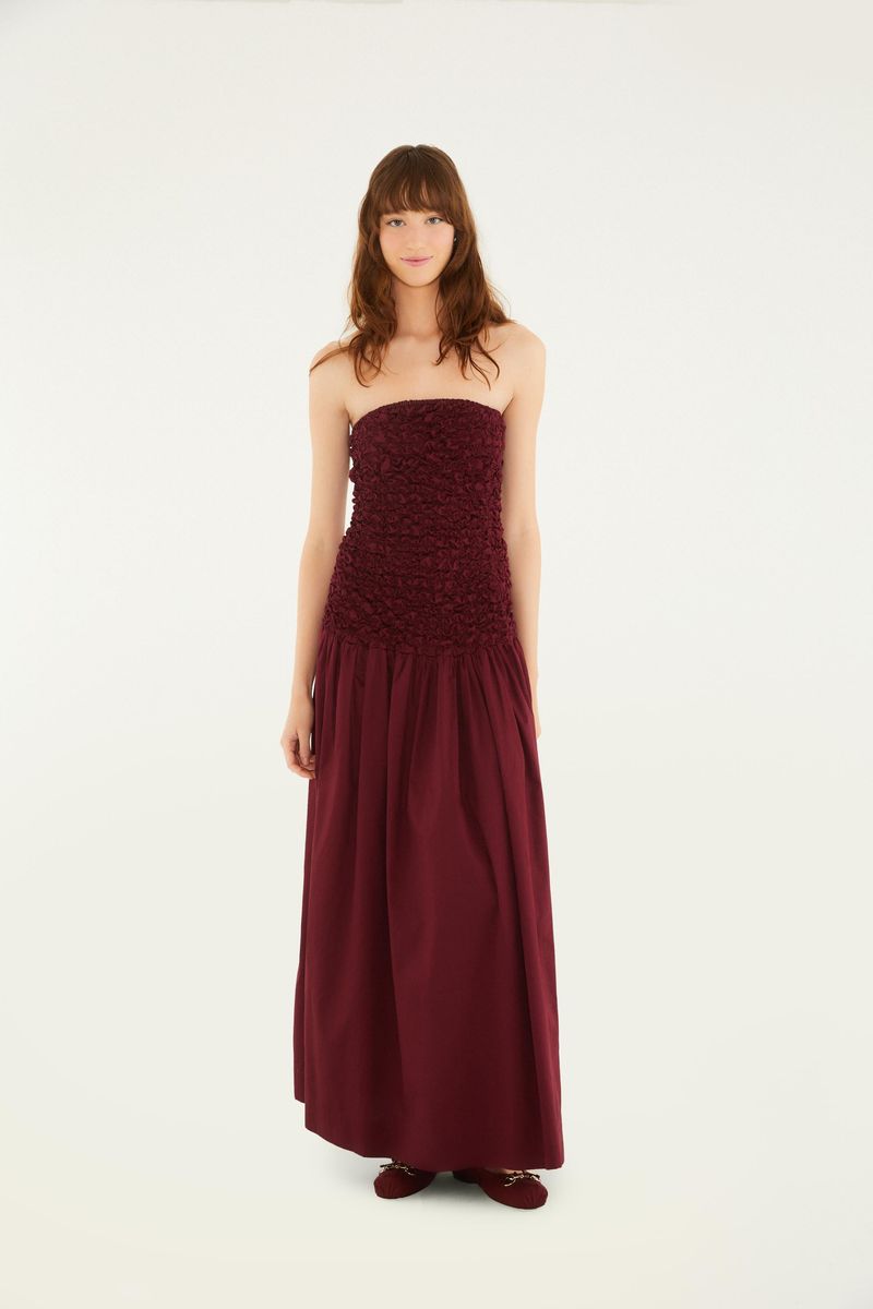Imagen de un vestido largo sin tirantes en tono vino, con detalle de lastex en el corpiño y falda fluida.