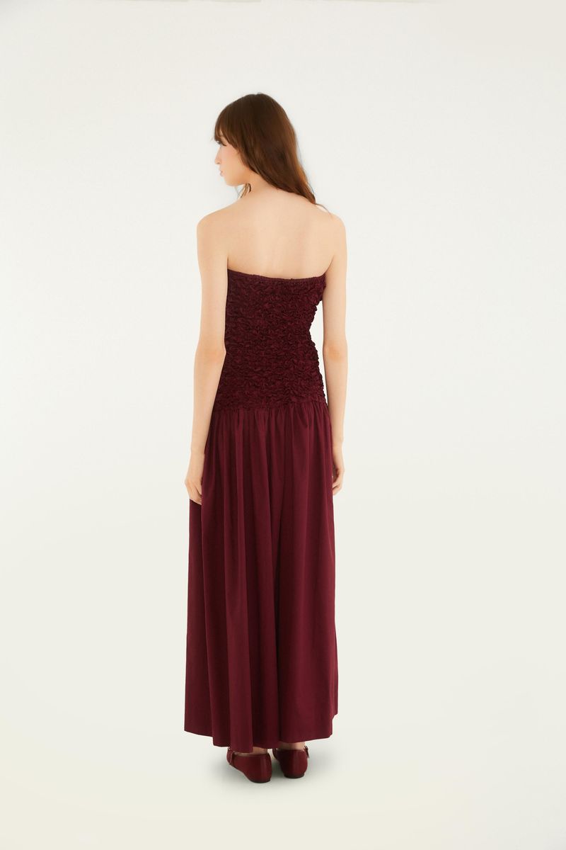 Vista trasera del vestido largo sin tirantes en tono vino, con detalle de lastex en el corpiño y falda fluida.