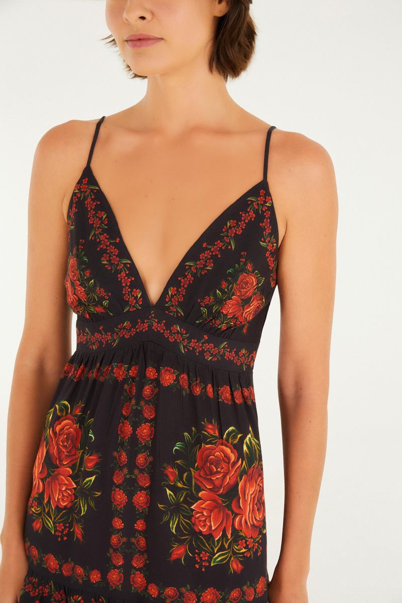 Imagen de un vestido con tirantes finos y estampado floral sobre fondo negro, mostrando detalles del dobladillo.