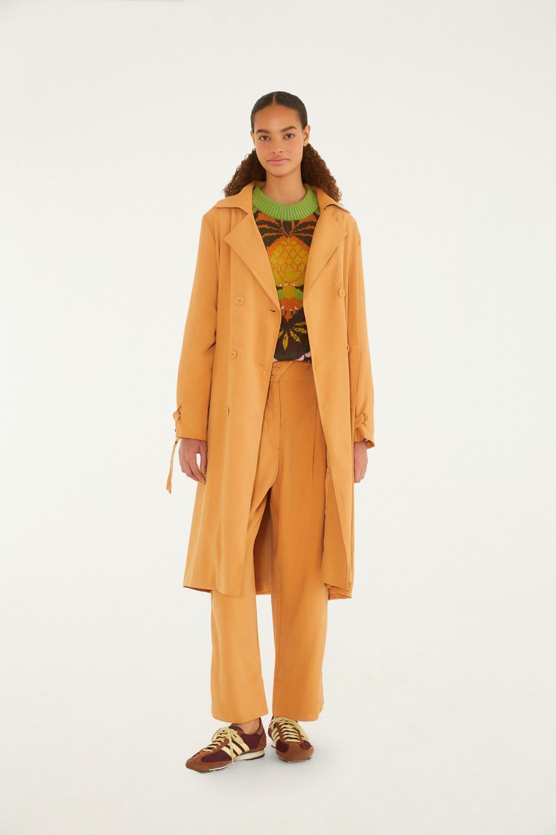 Modelo llevando trench coat ocre con pantalón combinado.