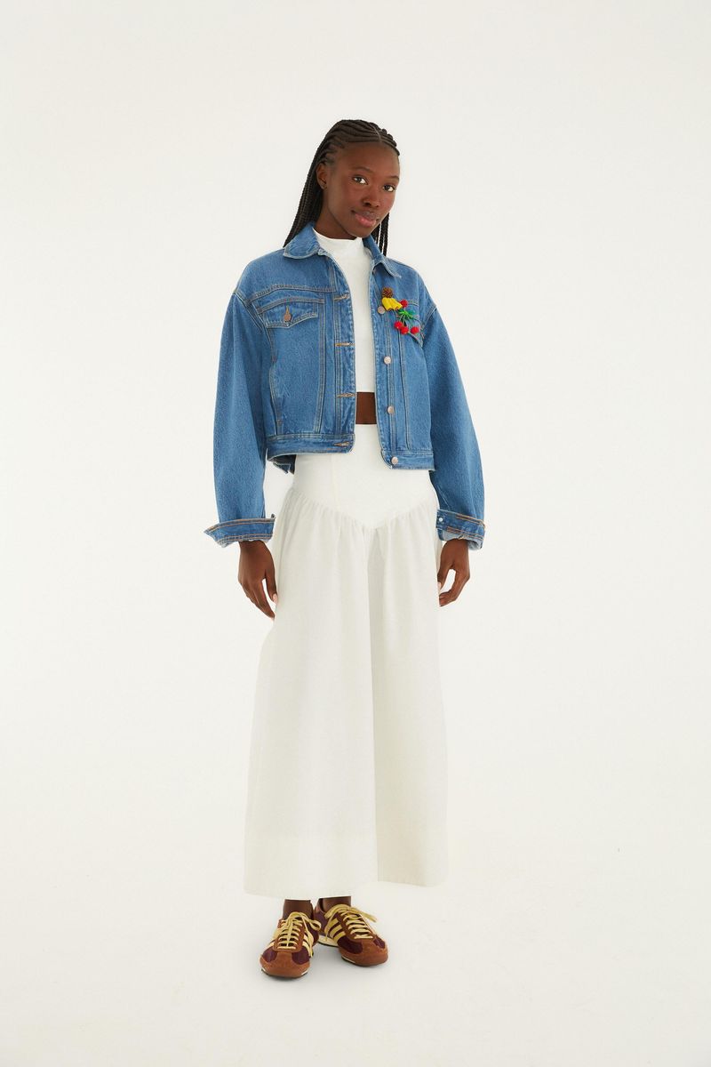 Modelo vistiendo blusa cropped blanca con falda larga y chaqueta de mezclilla.