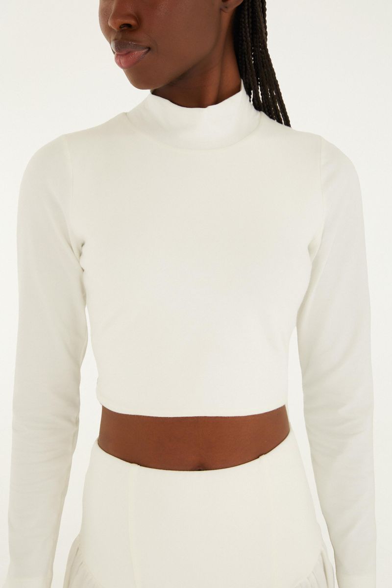 Detalle del cuello alto y mangas largas de la blusa cropped blanca.