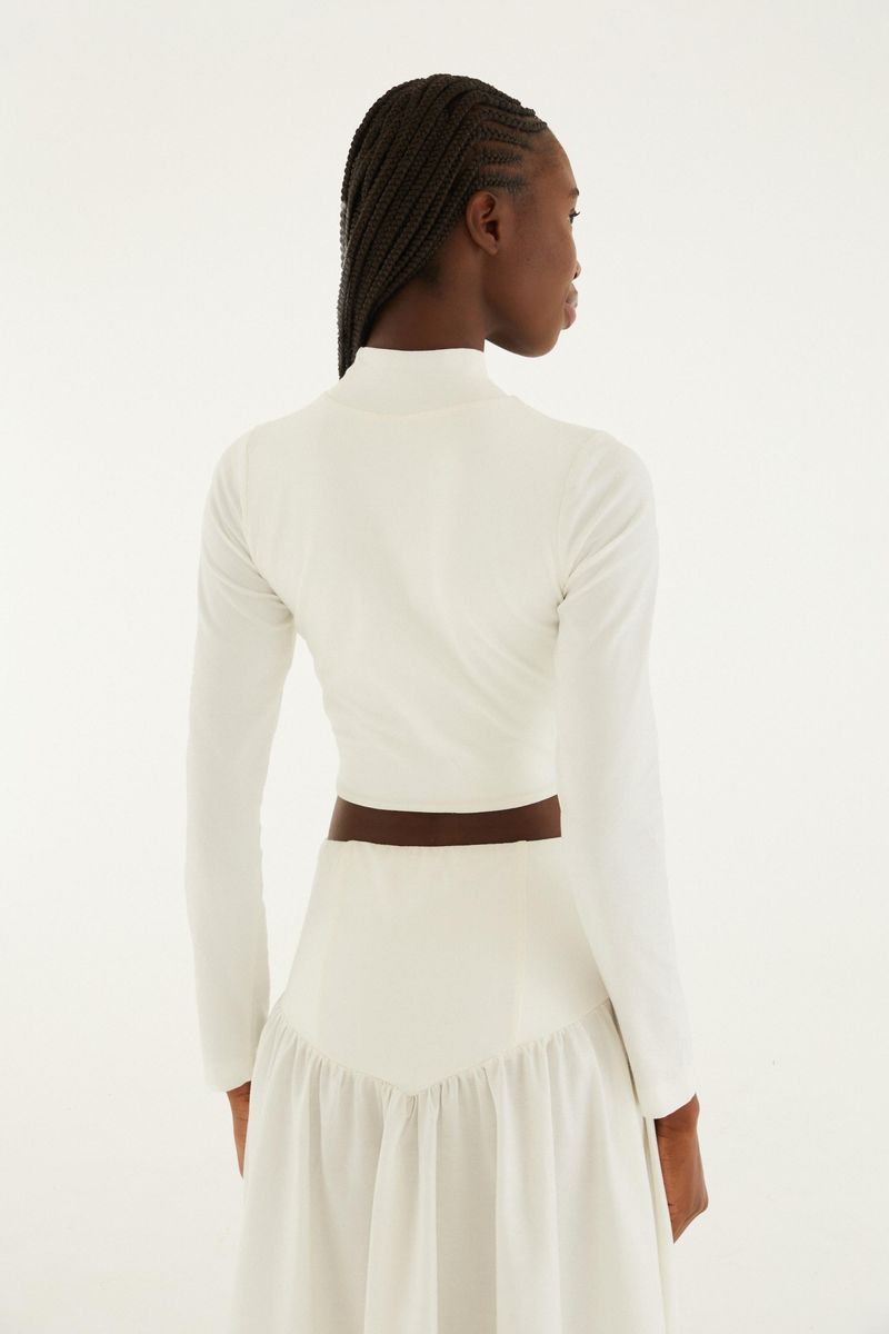 Vista trasera de la blusa cropped blanca con cuello alto y mangas largas.