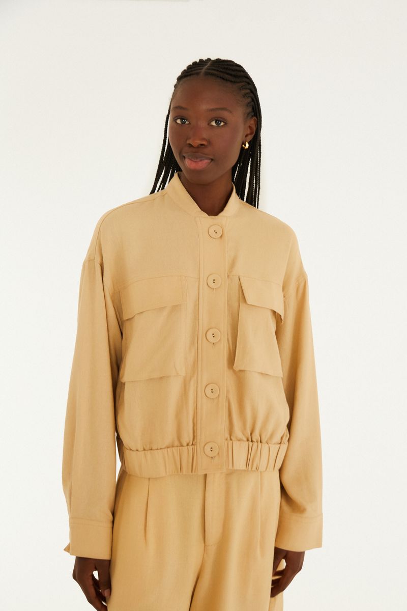 Chaqueta bomber beige vista desde el frente, con bolsillos frontales y cierre por botones.