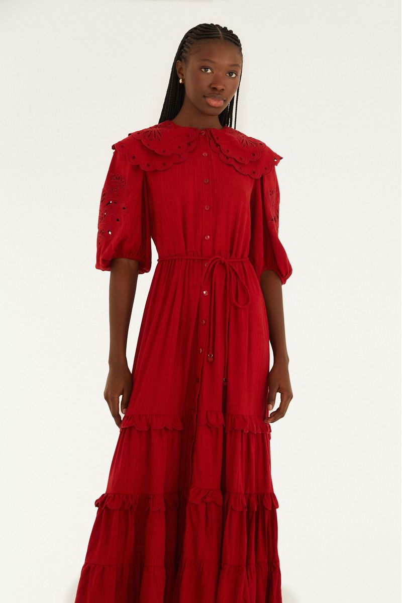 Acercamiento del vestido rojo con cuello bordado artesanal, destacando los detalles de las mangas abullonadas y el acabado de la barra en capas.