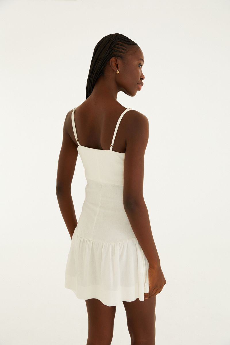 Vista trasera del vestido corto blanco crema con tirantes delgados y falda fluida.