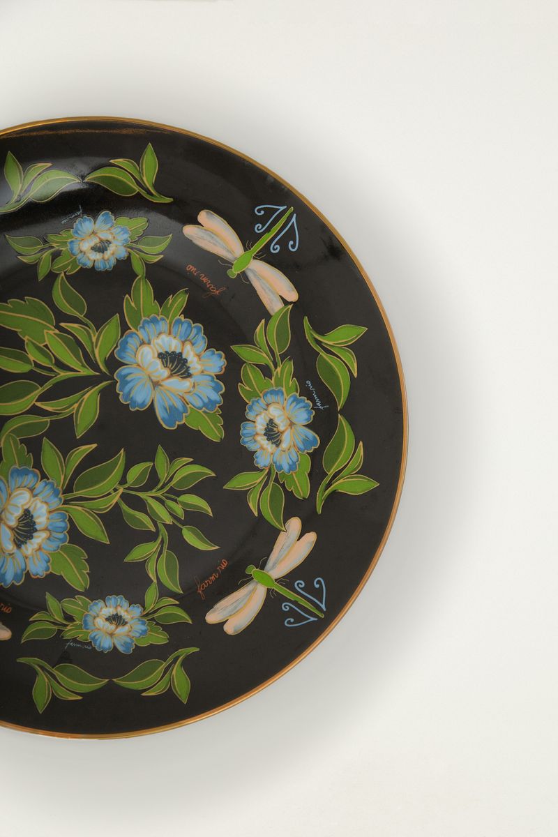 Plato llano con estampado de libélulas y flores azules en fondo negro, detalle del diseño.