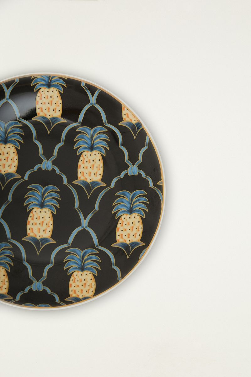 Plato de postre con estampado tropical de piñas en fondo negro, detalle ampliado.