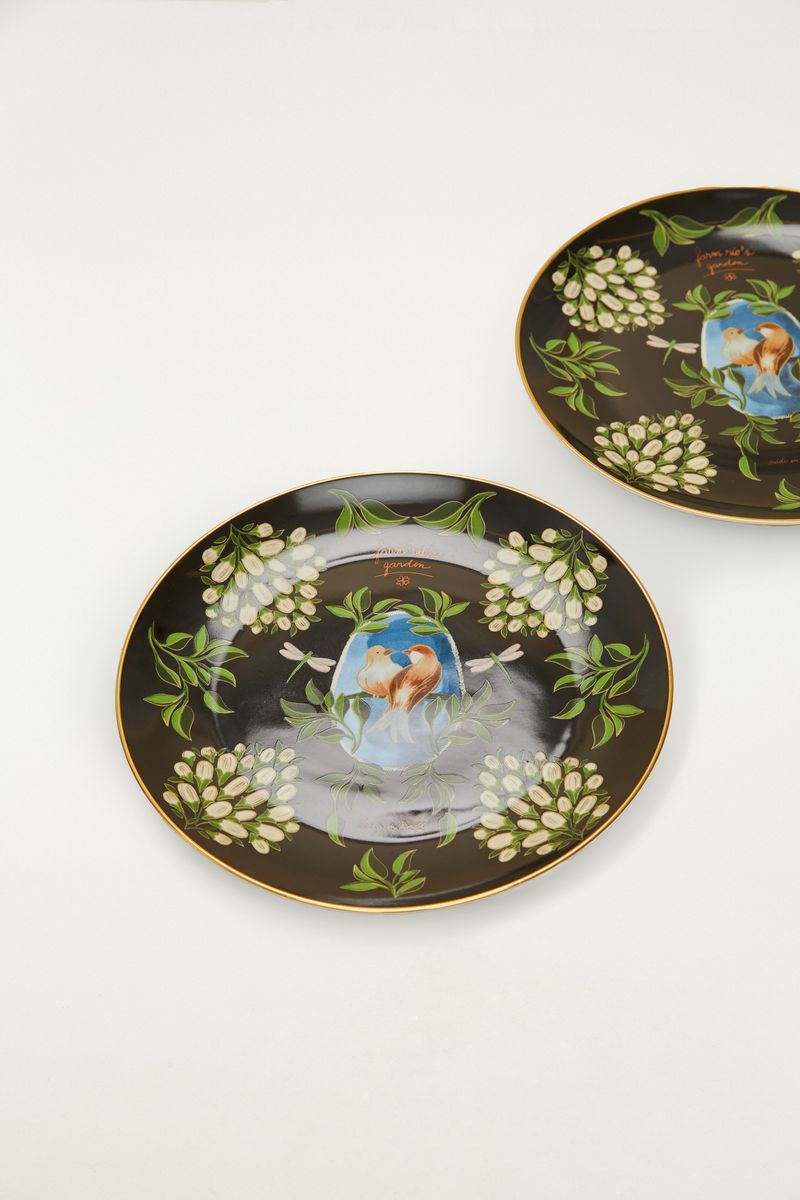 Plato de postre con diseño floral e ilustración de pájaro sobre fondo negro.
