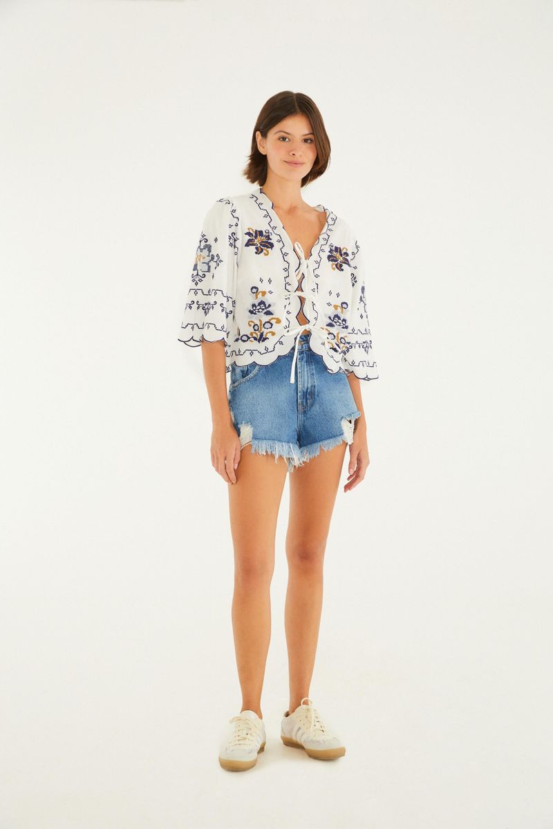 Modelo usando short de mezclilla dañado con hendidura baja y borde deshilachado, combinado con blusa estampada y tenis.