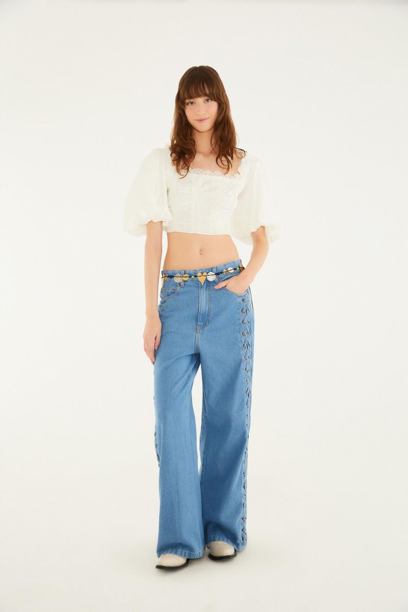 Imagen de una modelo usando un pantalón jean azul claro con detalles en el lateral y una blusa blanca de mangas abullonadas.