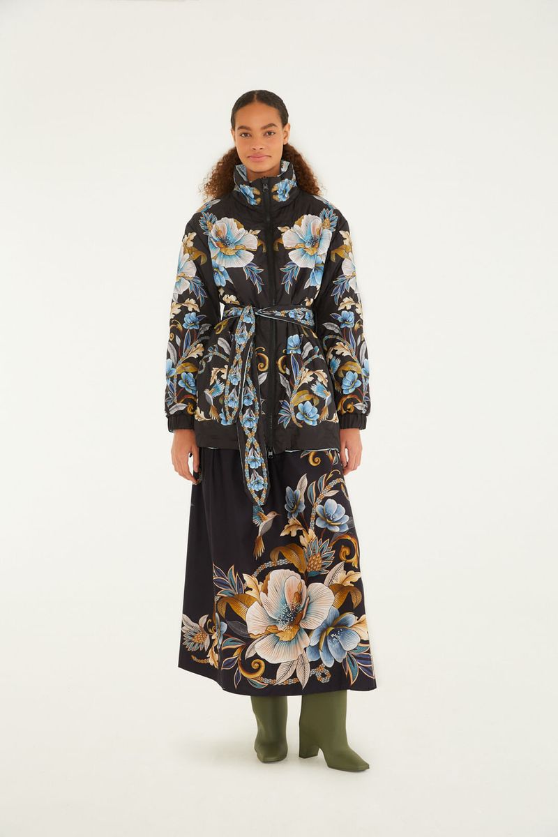 Modelo usando una falda corta con estampado floral vibrante en fondo negro, combinada con blusa del mismo estampado y botas verdes.