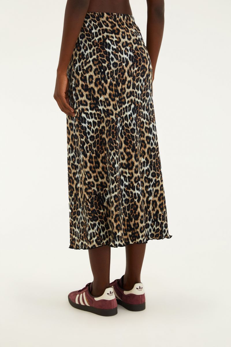 Modelo usando falda plisada midi con estampado de leopardo y zapatillas, creando un look casual.