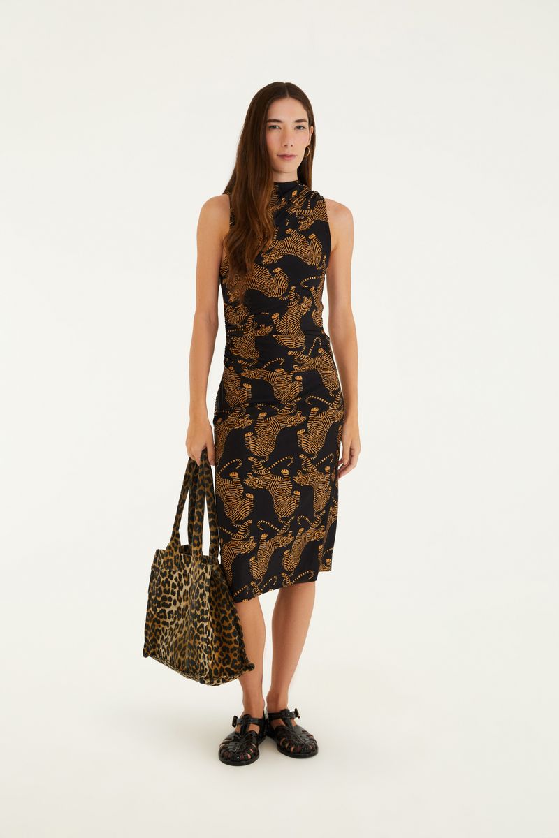 Modelo que lleva un vestido midi con estampado de tigres sobre fondo negro, sosteniendo una bolsa estampada.