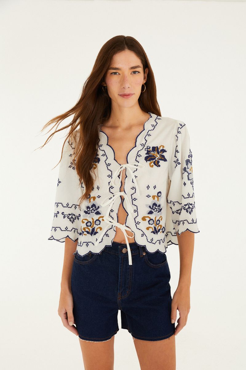 Modelo usando short de mezclilla azul oscuro con cintura alta y dobladillo aplicado, combinado con una blusa blanca bordada.