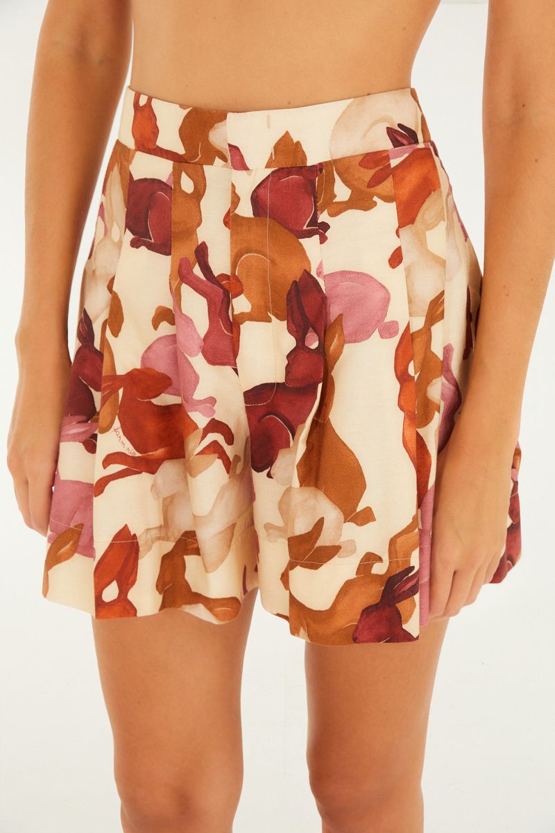Primer plano del frente de la bermuda con pliegues y estampado de conejos en tonos beige, marrón y rosado.