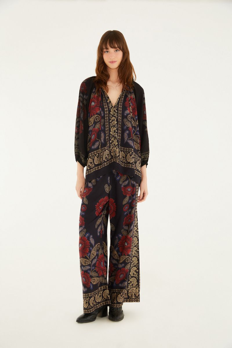 Imagen de una modelo vistiendo un pantalón estampado estilo palazzo con diseño floral en tonos rojos y dorados sobre fondo negro.