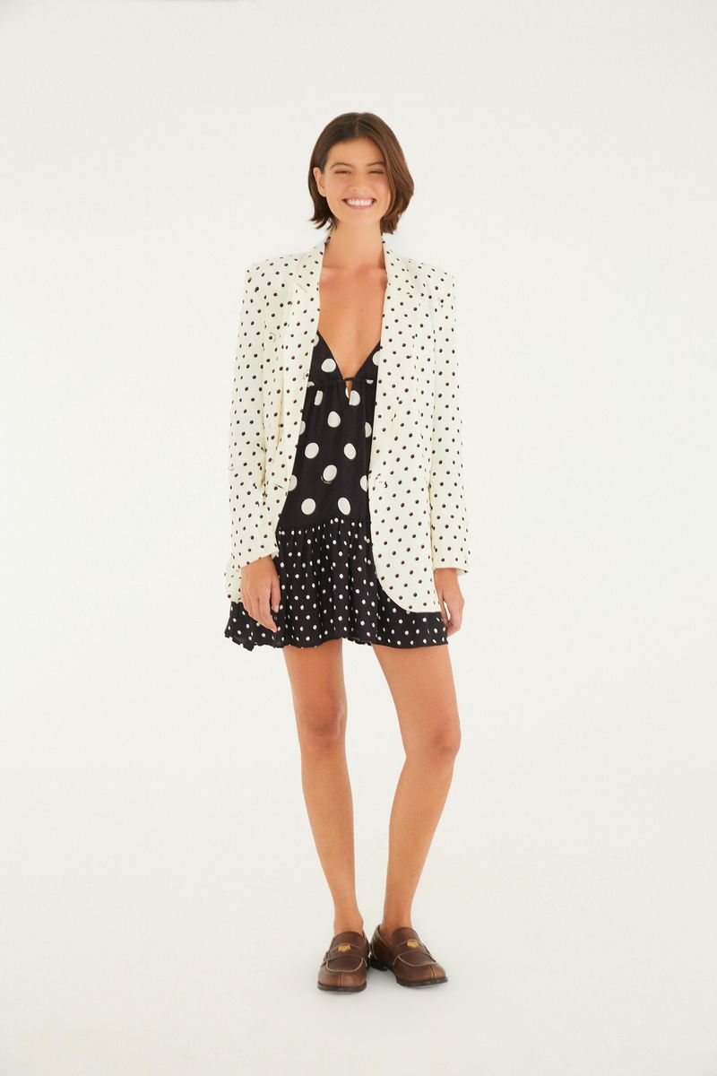 Modelo vistiendo el vestido corto con estampado de lunares, combinado con un blazer blanco y zapatos marrones.
