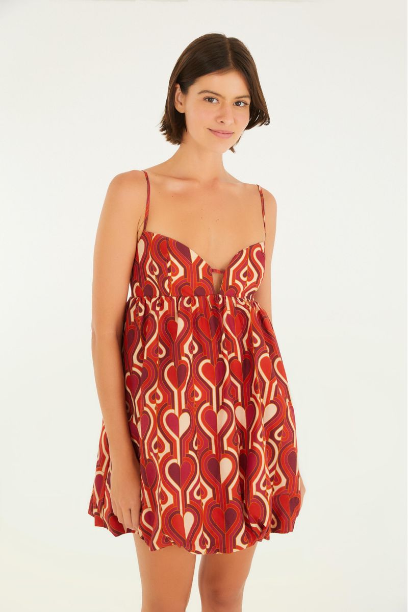 Vestido corto estampado con patrón geométrico en tonos rojos y blancos, visto de frente, con tirantes finos y escote en V.