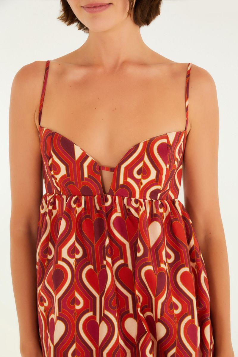 Detalle del vestido corto estampado con patrón geométrico en tonos rojos y blancos, mostrando el escote en V y los tirantes finos.