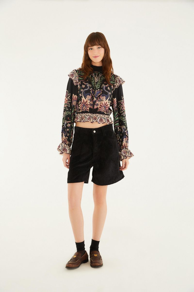 Imagen de una modelo usando una bermuda de cotelé negra con una blusa estampada, vista frontal.