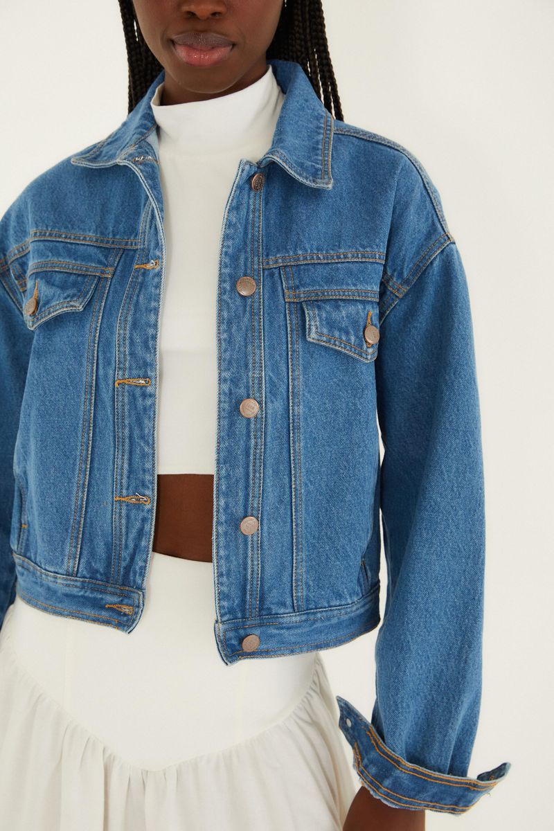 Detalle de la chaqueta cropped en denim azul con bolsillos de solapa y cierre con botones.