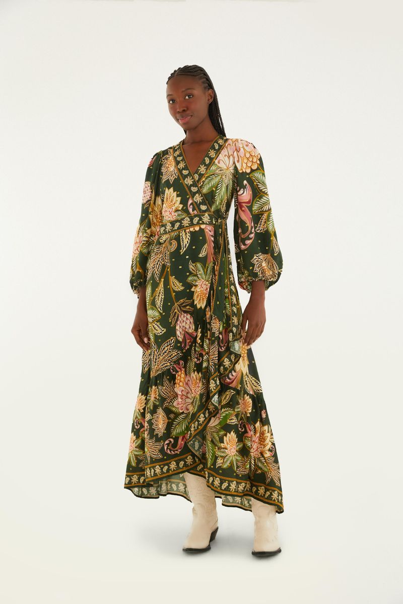 Modelo lleva un vestido largo con estampado floral sobre fondo verde, mangas abuchonadas y escote en V.