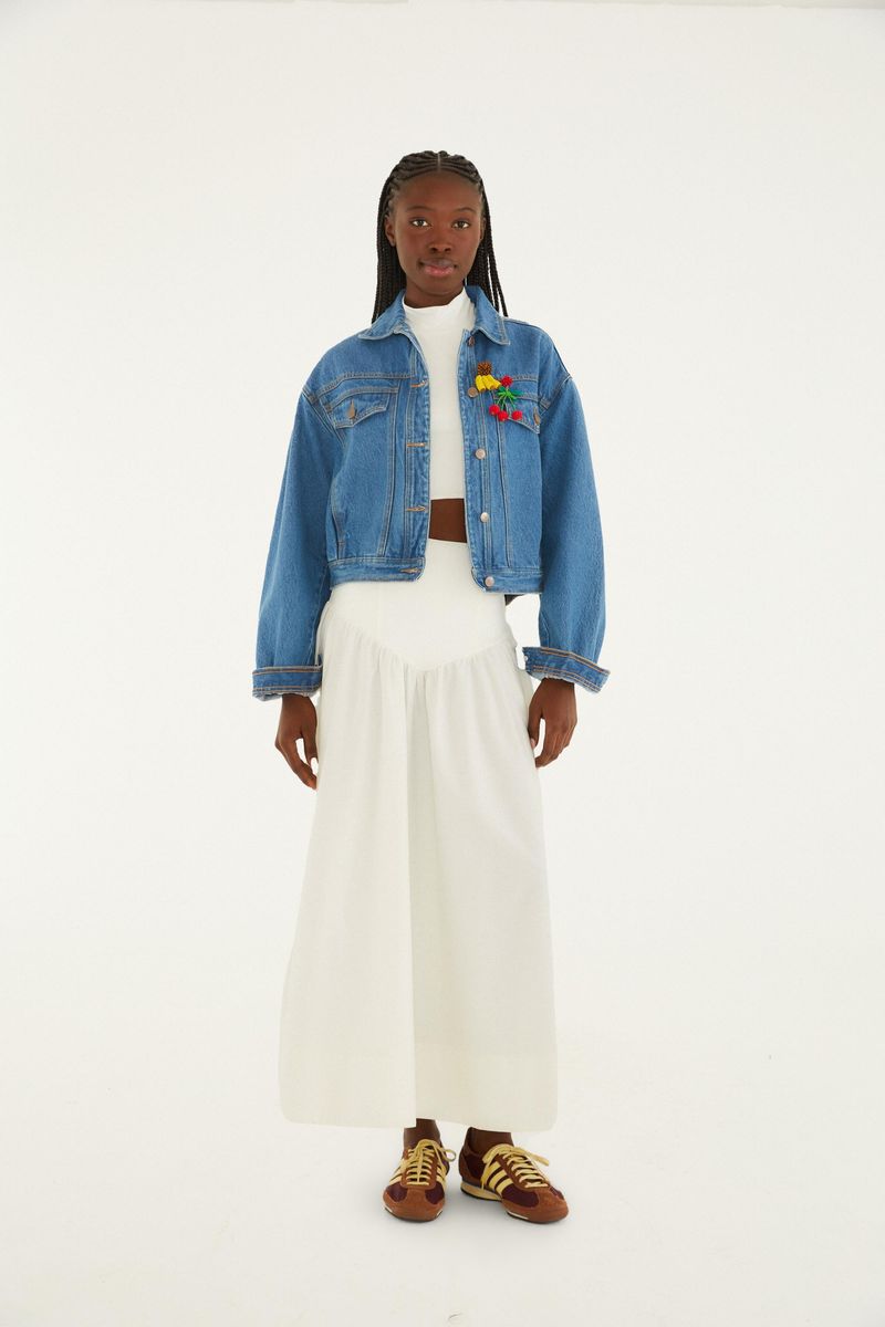 Chaqueta cropped en denim azul con mangas largas, combinada con falda blanca, vista completa.