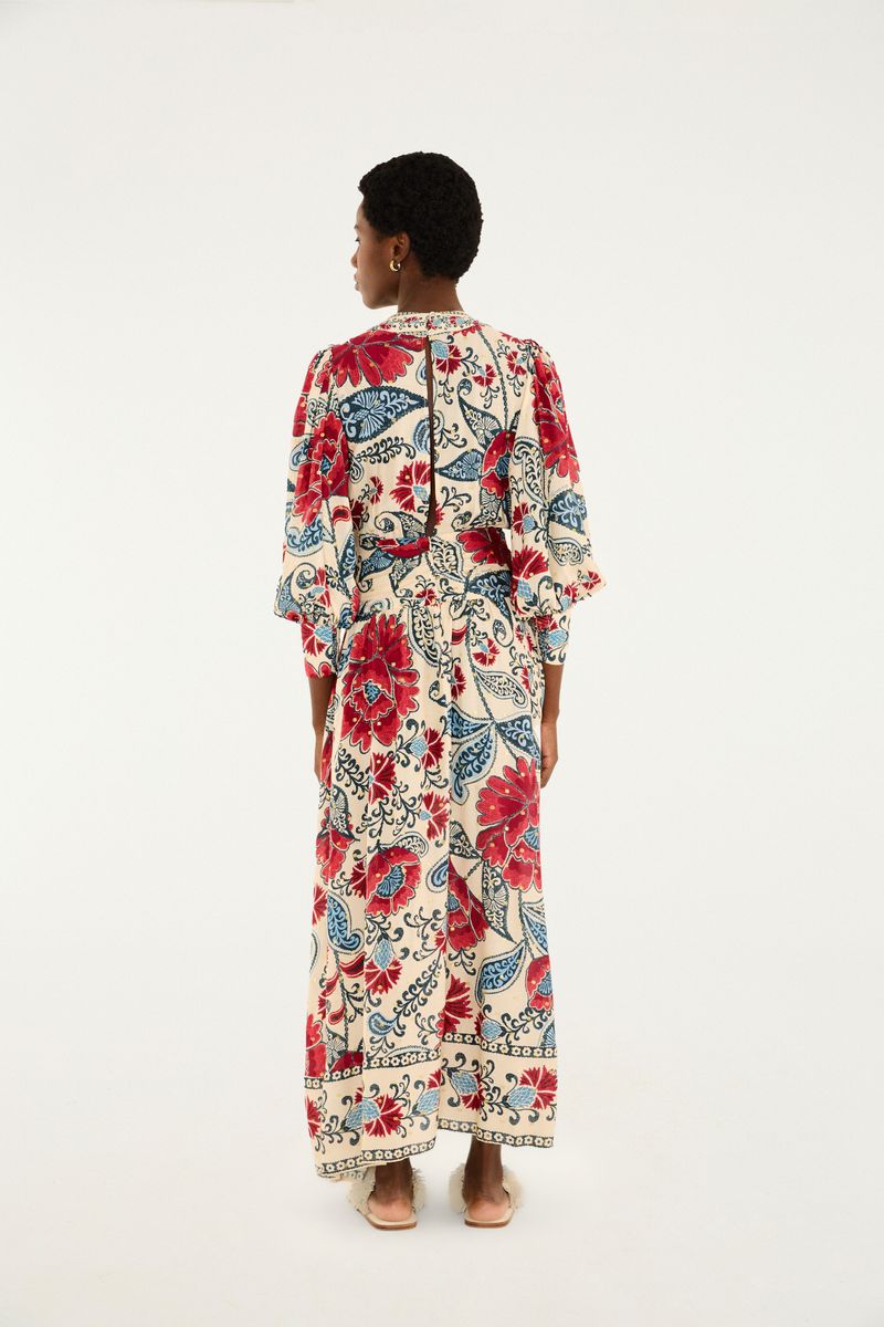 Imagen de un vestido largo con mangas abullonadas y estampado floral en tonos de rojo y azul sobre fondo beige, visto de espaldas.