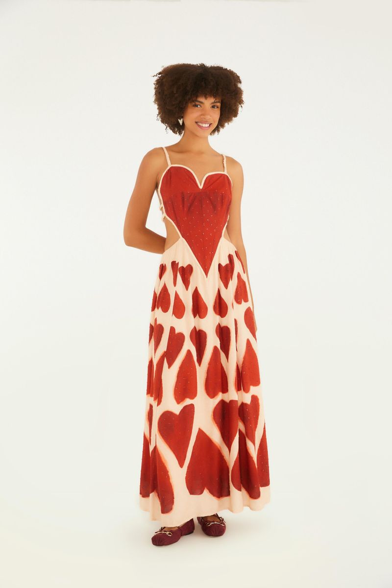 Vestido maxi con estampado de corazones rojos sobre fondo beige, tirantes finos y escote en forma de corazón.