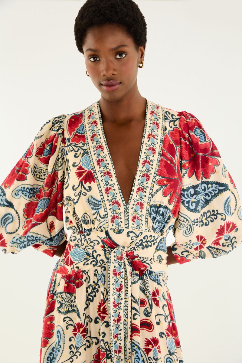 Imagen de un vestido largo con mangas abullonadas y estampado floral en tonos de rojo y azul sobre fondo beige, con detalle del escote en V.