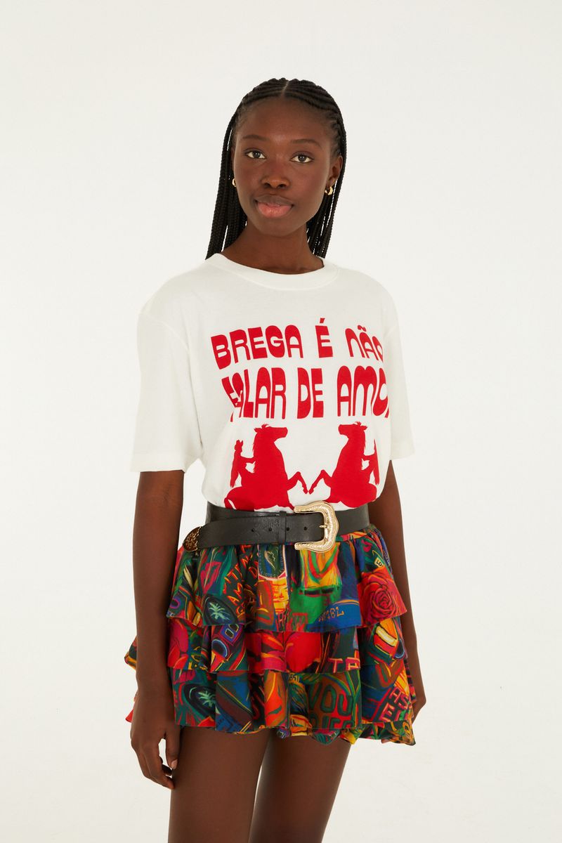 Modelo usando una falda corta con volantes y estampado colorido, combinada con camiseta blanca estampada y cinturón negro.