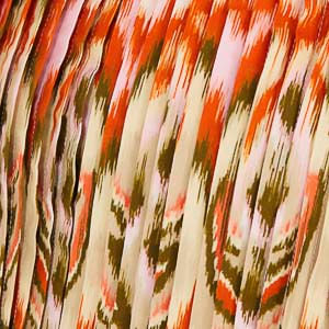 Imagen de un vestido largo con tirantes, estampado con patrón Ikat en tonos naranja, verde y blanco, visto desde el lado.