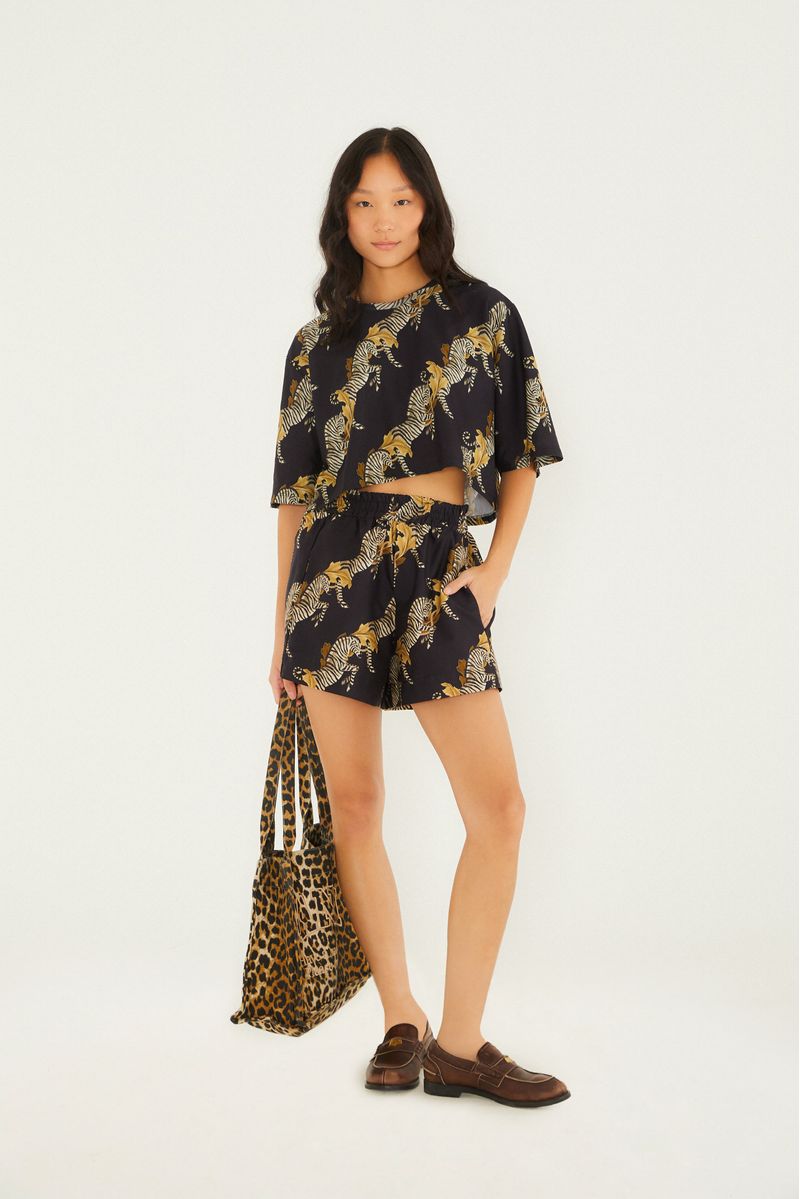 Modelo usando un conjunto de short y blusa estampados con tema de cebra, sosteniendo una bolsa.