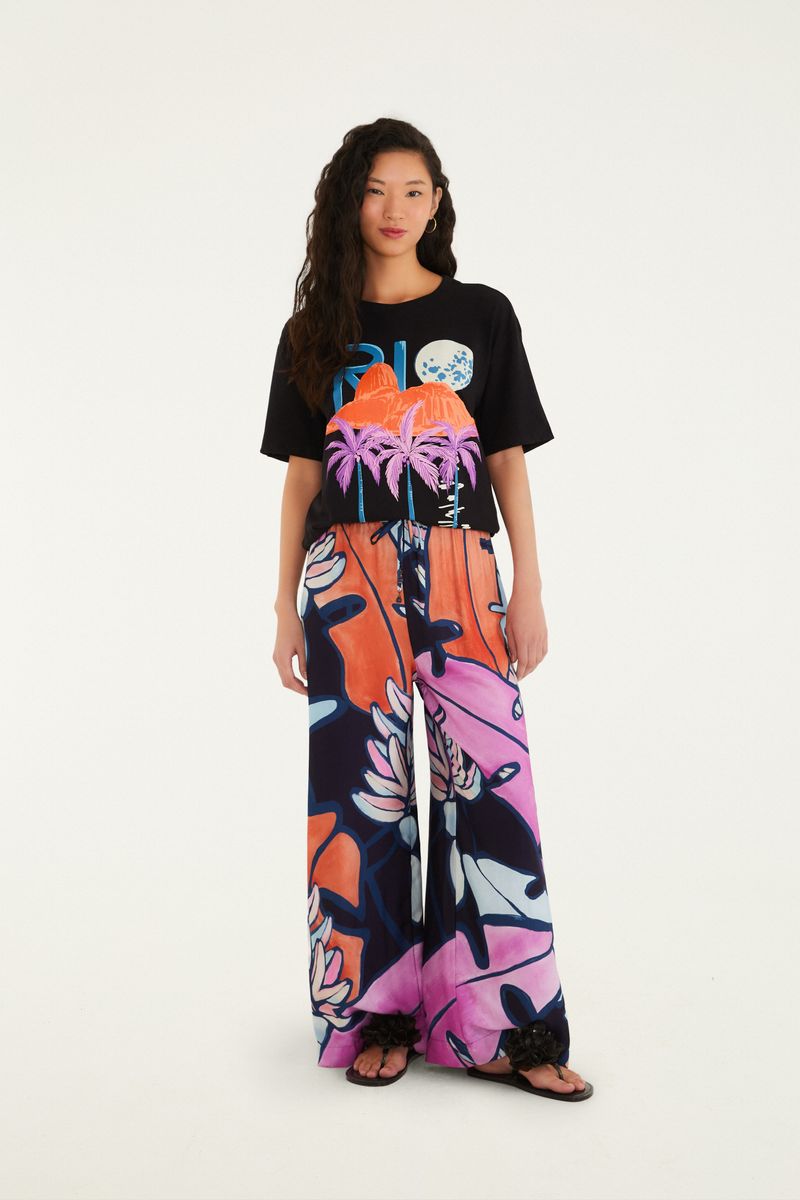 Modelo usando camiseta negra con estampado tropical, combinada con pantalón estampado.