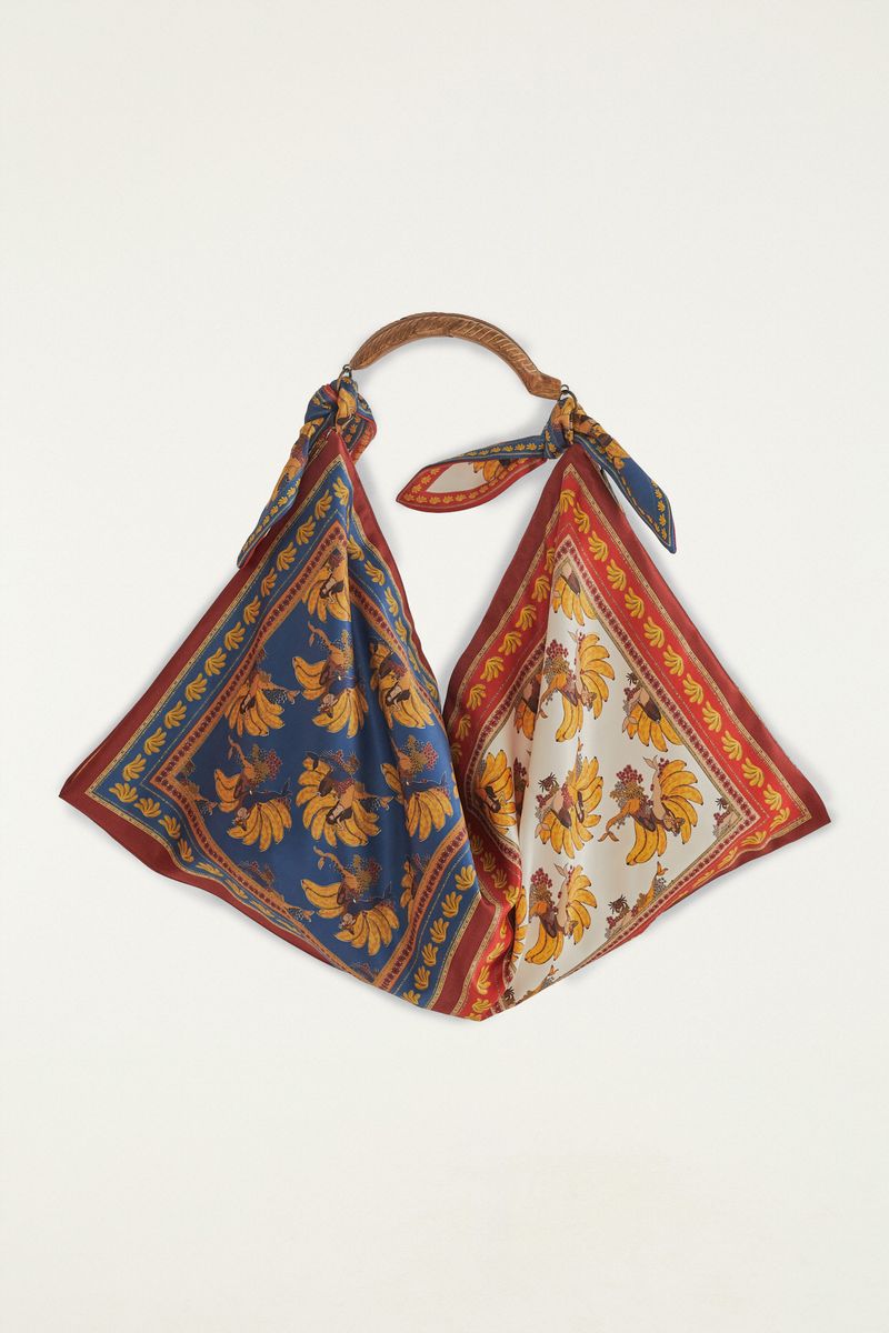 Bolsa Mini Sereia Banana con estampados tropicales sobre fondo azul y blanco, con asas de madera.