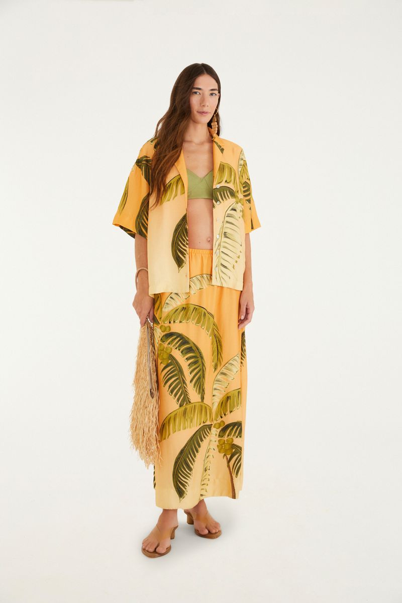 Modelo vistiendo camisa tropical con estampado de palmeras, combinada con falda.