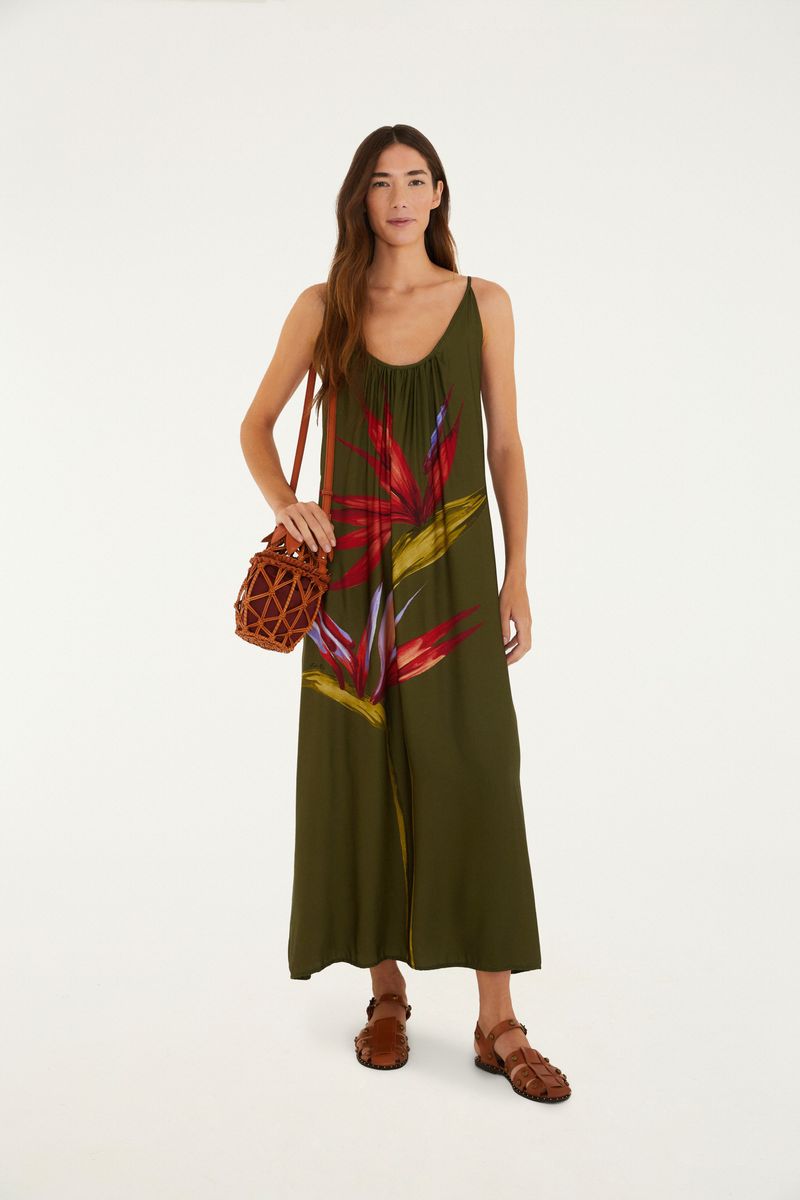Modelo usando un vestido largo maxi con estampado de flores sobre fondo verde, lleva un bolso de paja.