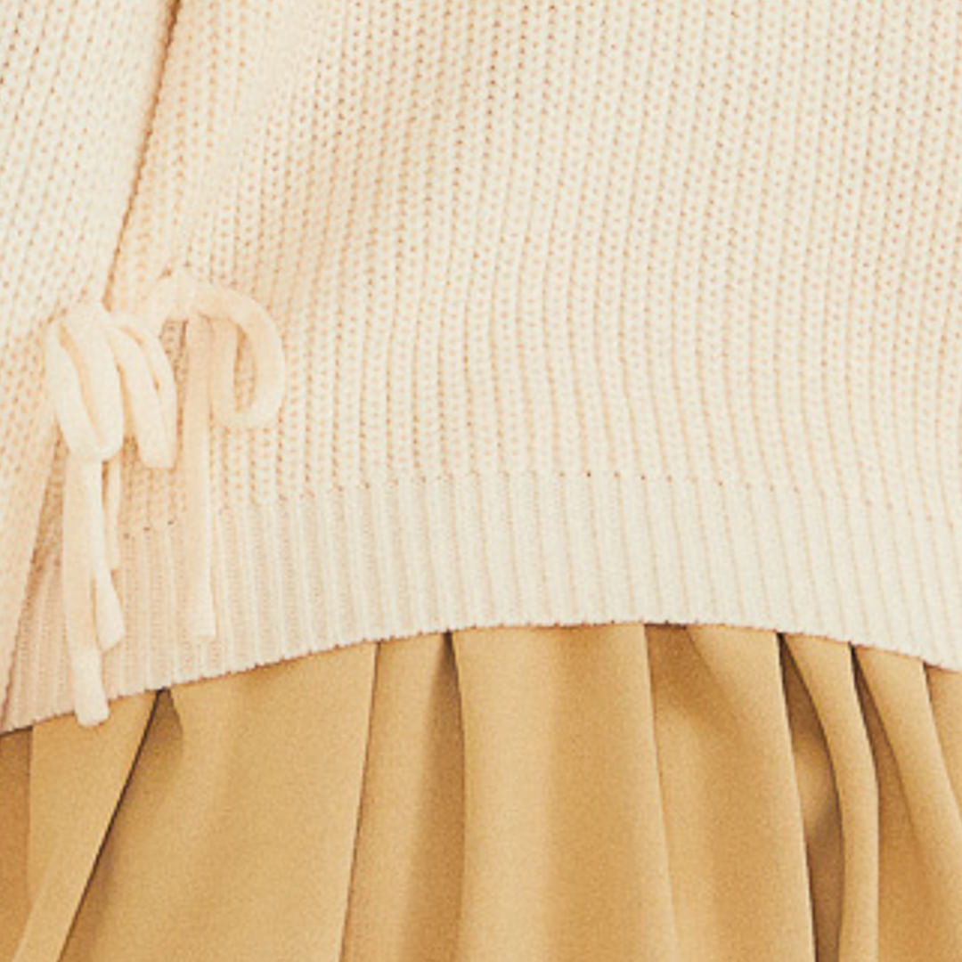 Primer plano de los lazos y la textura del tricot beige del cárdigan.