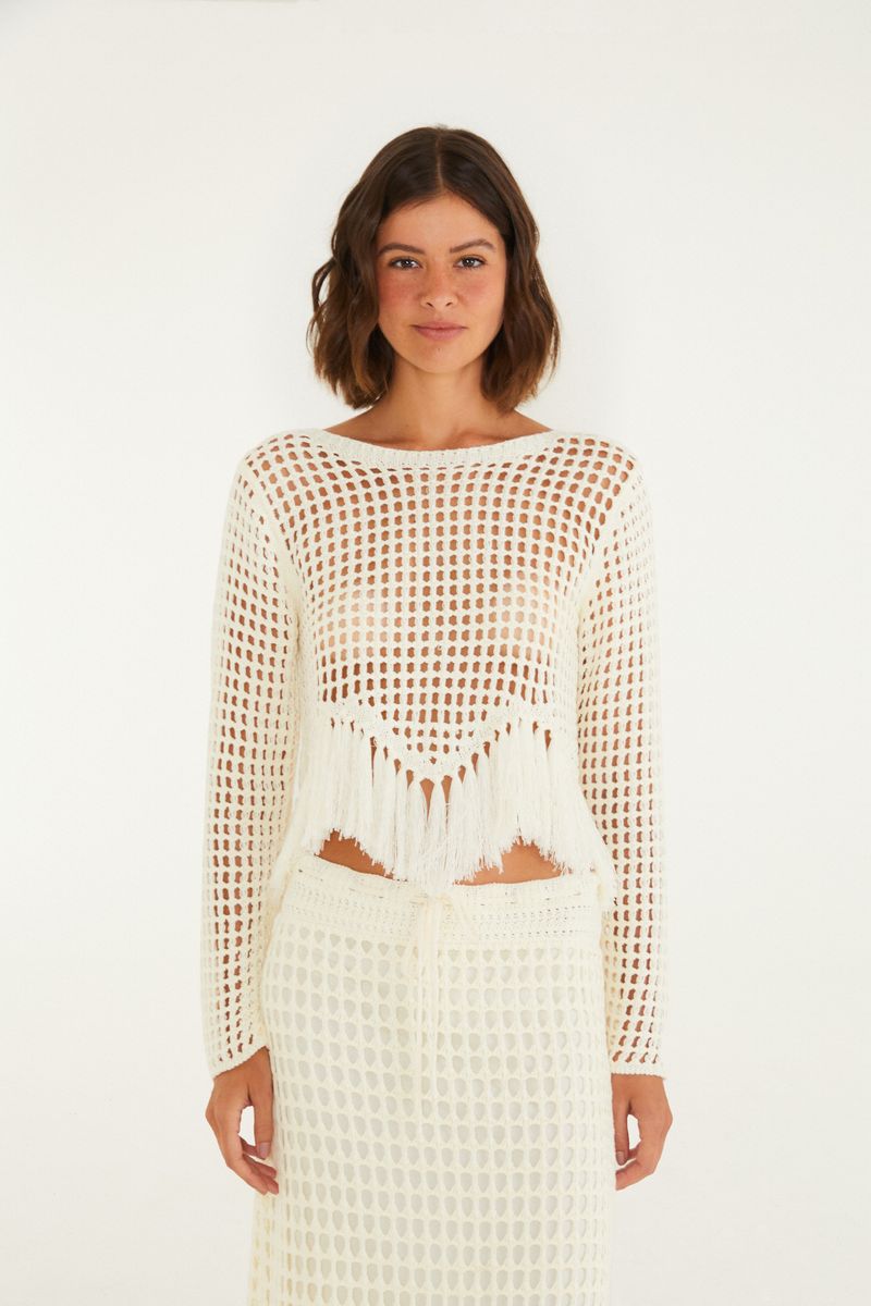 Detalle de la blusa de tejido beige con flecos, mostrando el patrón y la textura.
