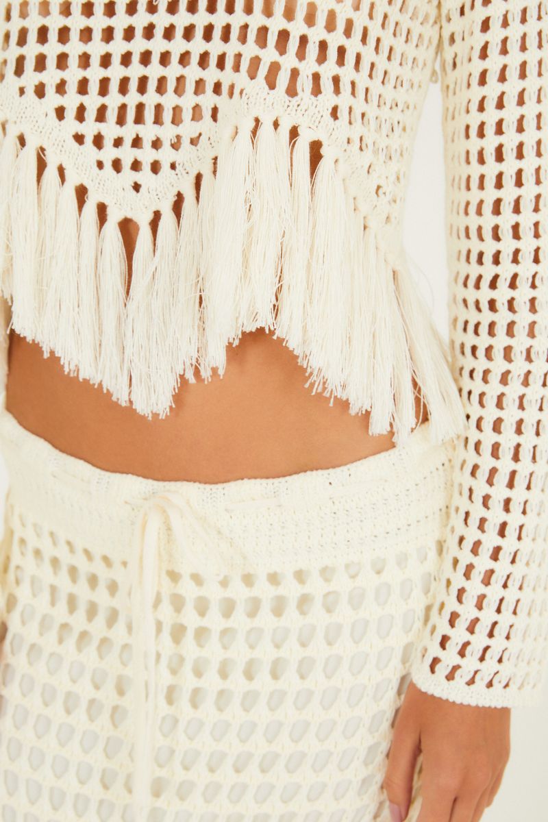 Close-up del detalle del fleco en la blusa de tejido beige.