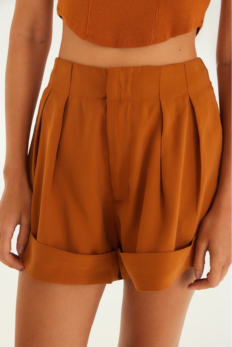Close-up del short de alfaiataria color ocre mostrando los detalles de la cintura y dobladillo.