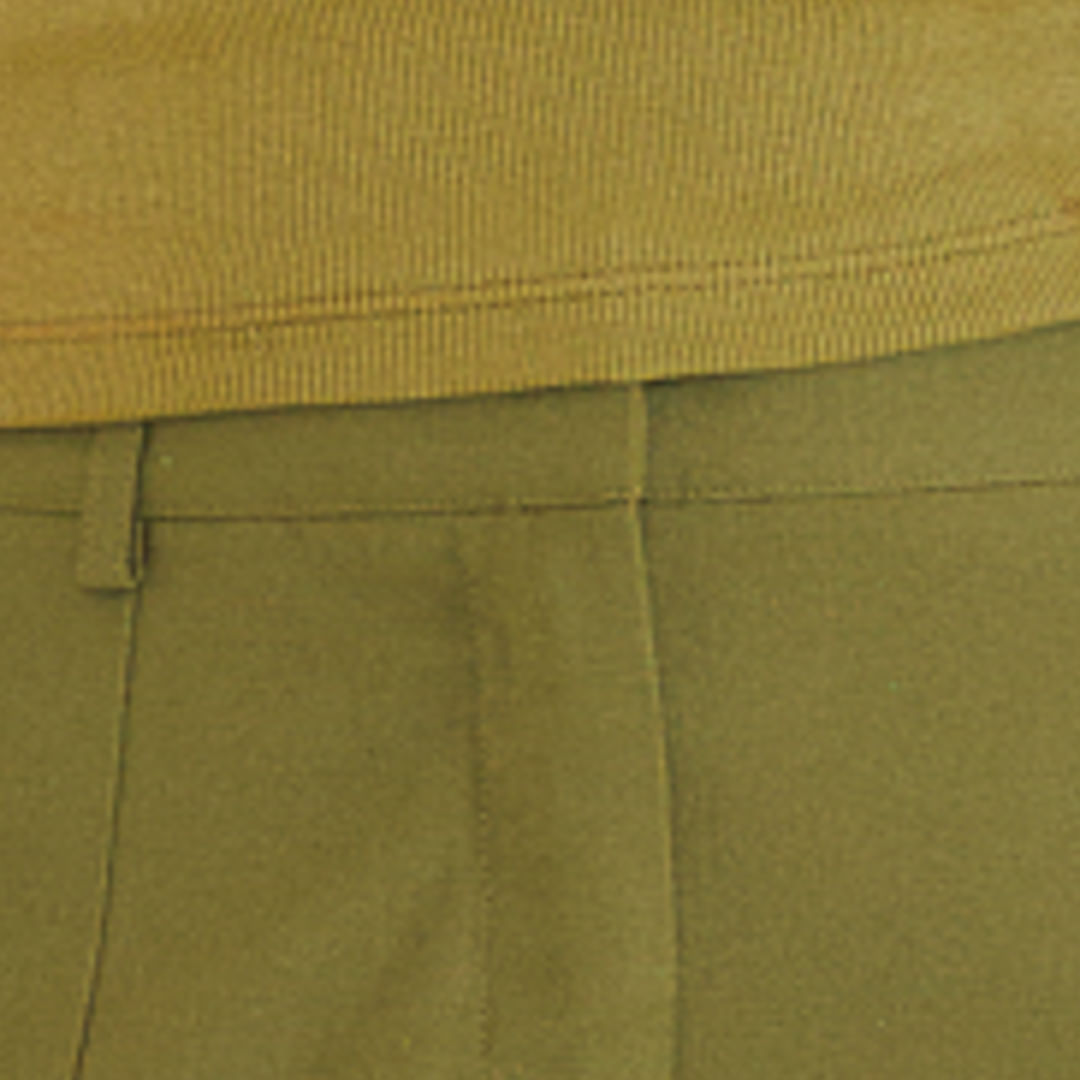 Close-up de la pretina y cierre con botón del pantalón de sastrería verde.