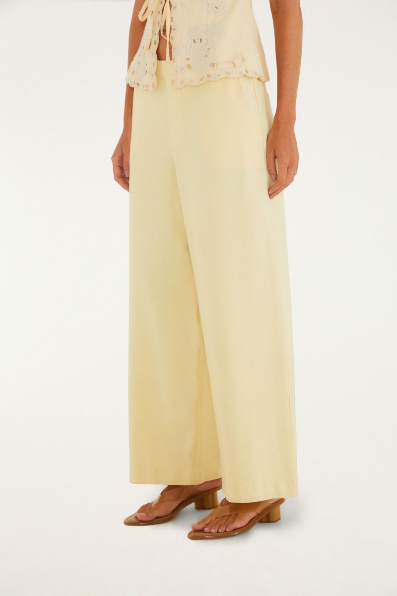Imagen lateral de la modelo mostrando el pantalón ancho en color beige con detalles de la cintura.
