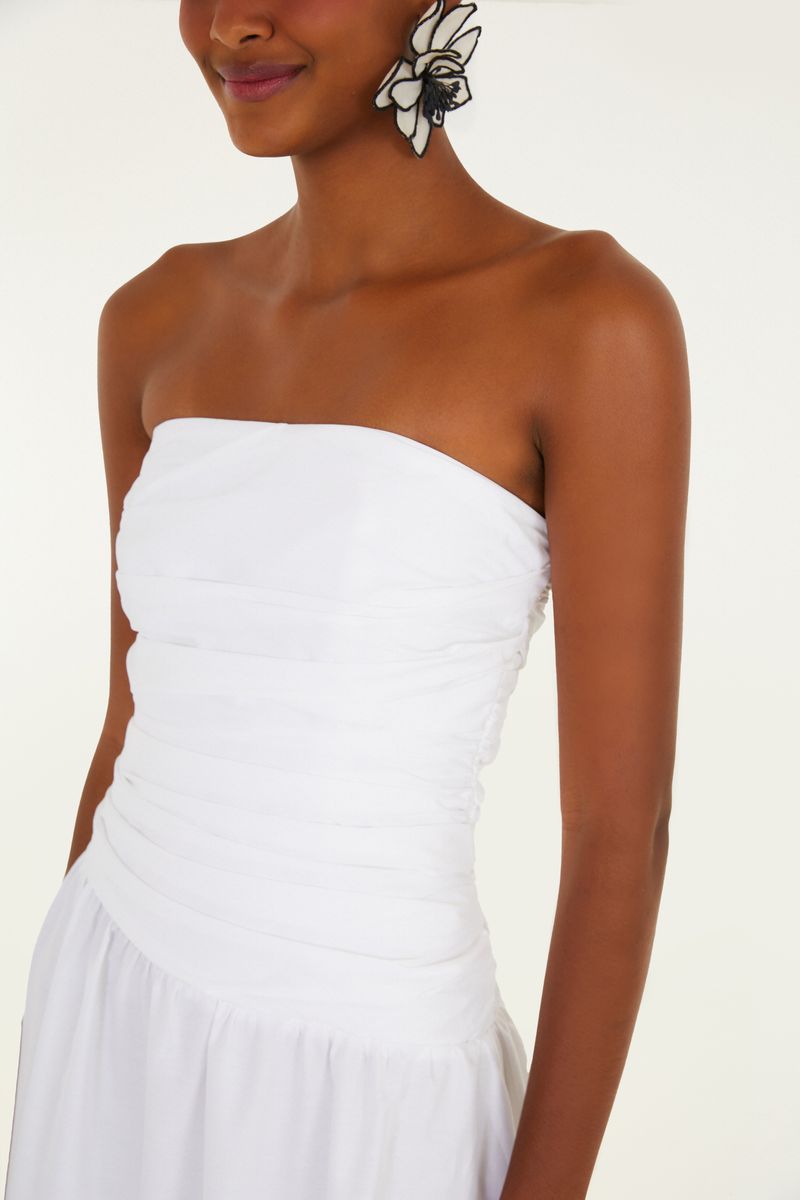 Imagen de un vestido sin tirantes blanco con fruncidos en la parte superior y falda larga en capas, visto de espaldas.