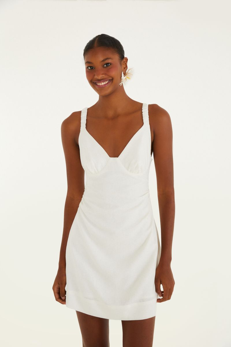 Modelo usando un vestido corto blanco con tirantes finos y escote en V, visto de frente.