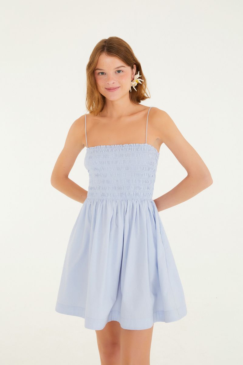 Vestido corto azul claro con elástico en la parte superior y cargaderas delgadas, visto de espaldas.