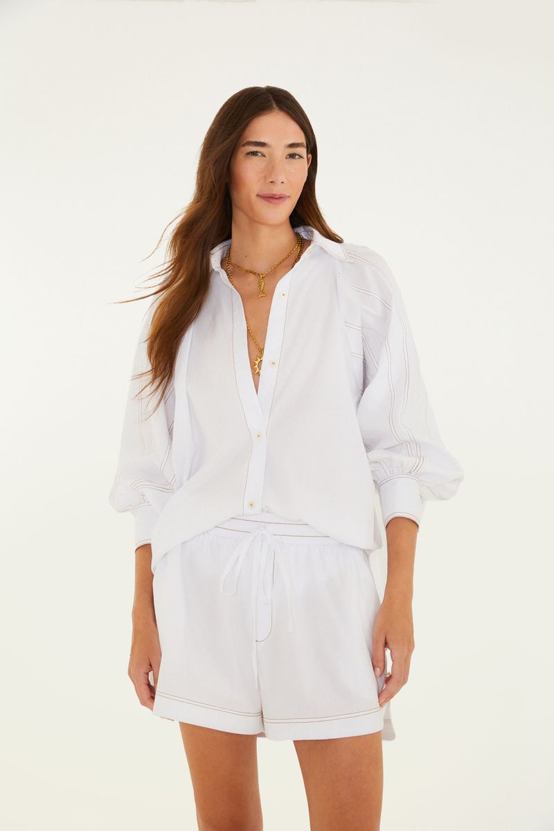 Camisa blanca con mangas abullonadas y pespuntes contrastantes, vista frontal.