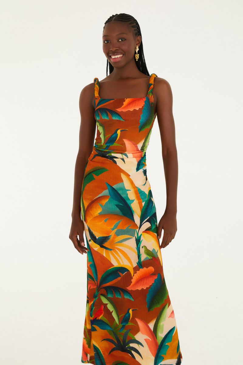 Modelo usando vestido largo con estampado tropical sobre fondo naranja, vista trasera.