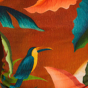 Acercamiento de la estampado tropical del vestido mostrando hojas y aves sobre fondo naranja.